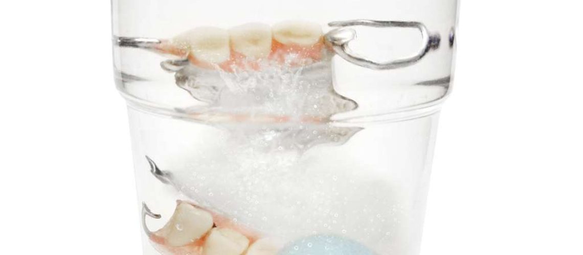 False Teeth in a glass with cleaning tablets and water glass "isolated on white"