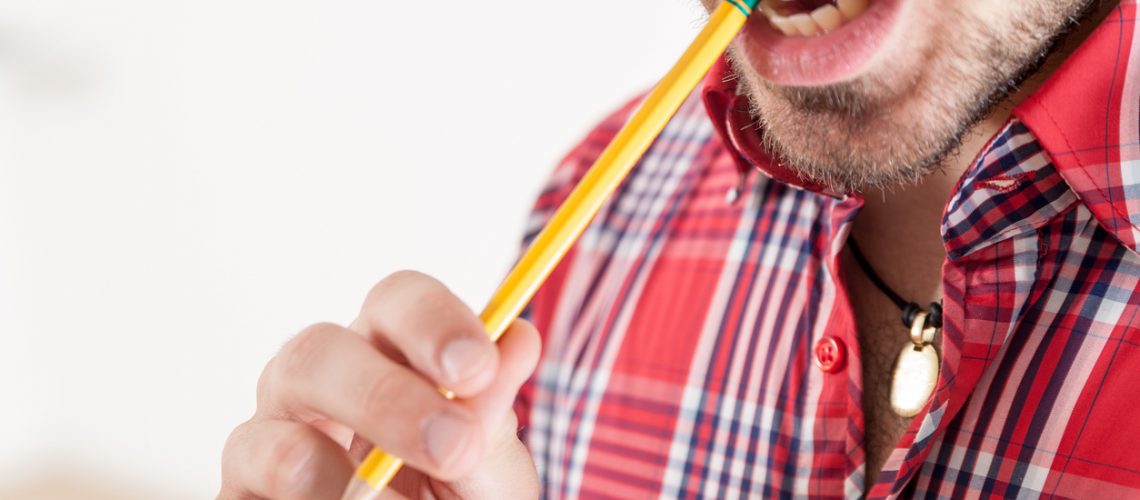 bearded man on a red checked shirt biting a pencil until a solution has been found and there is lots of copyspace